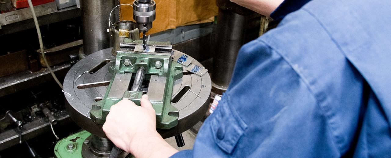 "従業員の肩越しに撮影した、部品に穴あけ作業をしている様子"